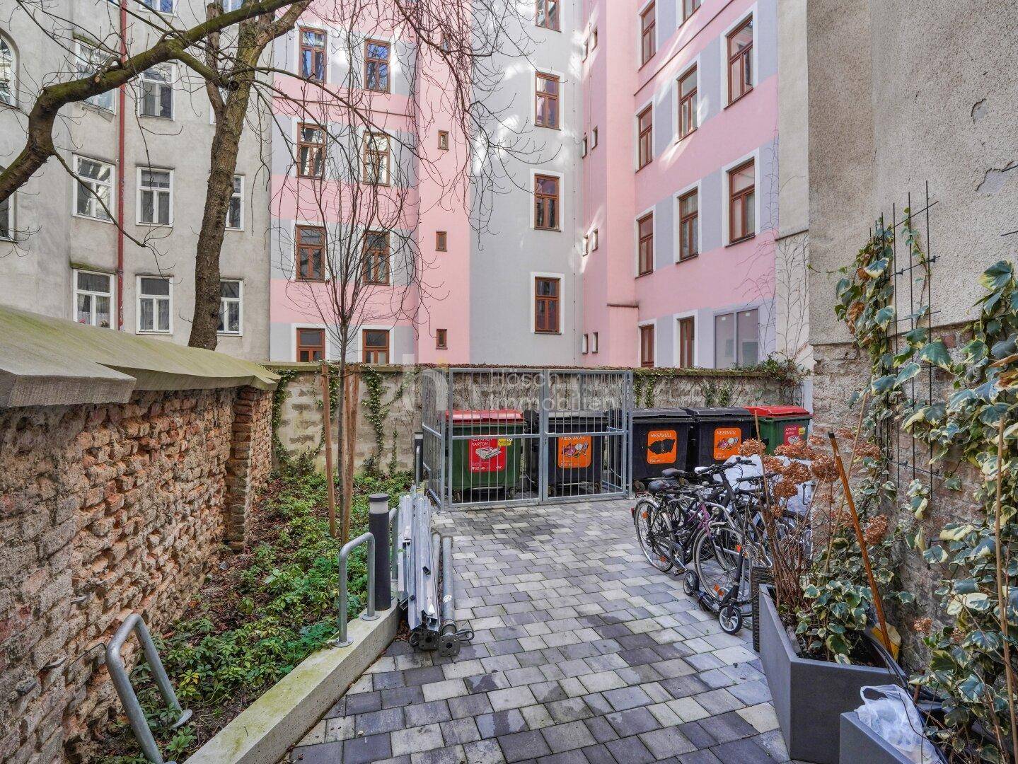 Innenhofbereich mit Fahrradabstellplätzen und Mülltonnen, umgeben von Gebäuden.
