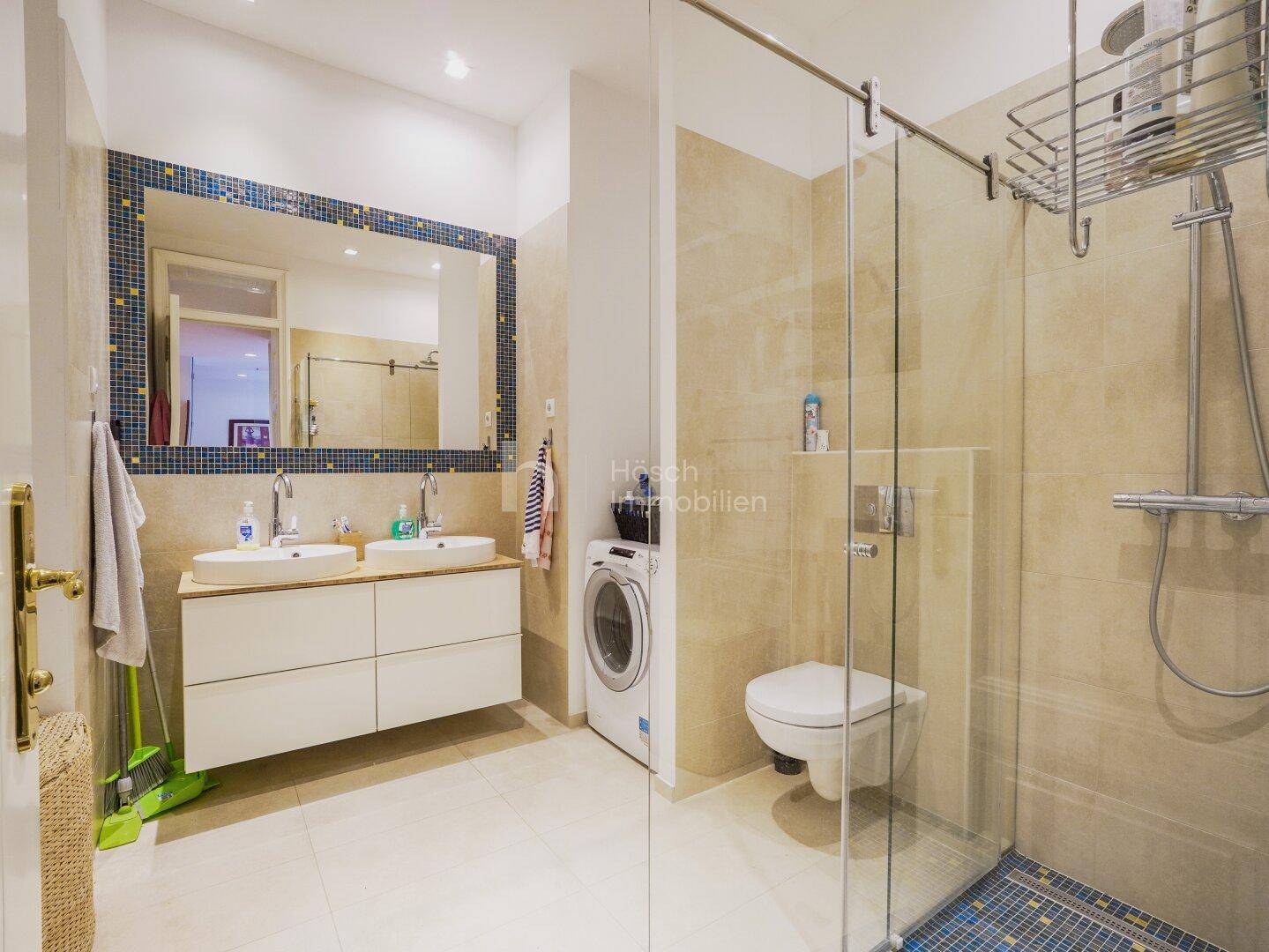 Modernes Badezimmer mit begehbarer Dusche, Doppelwaschbecken und integrierter Waschmaschine.