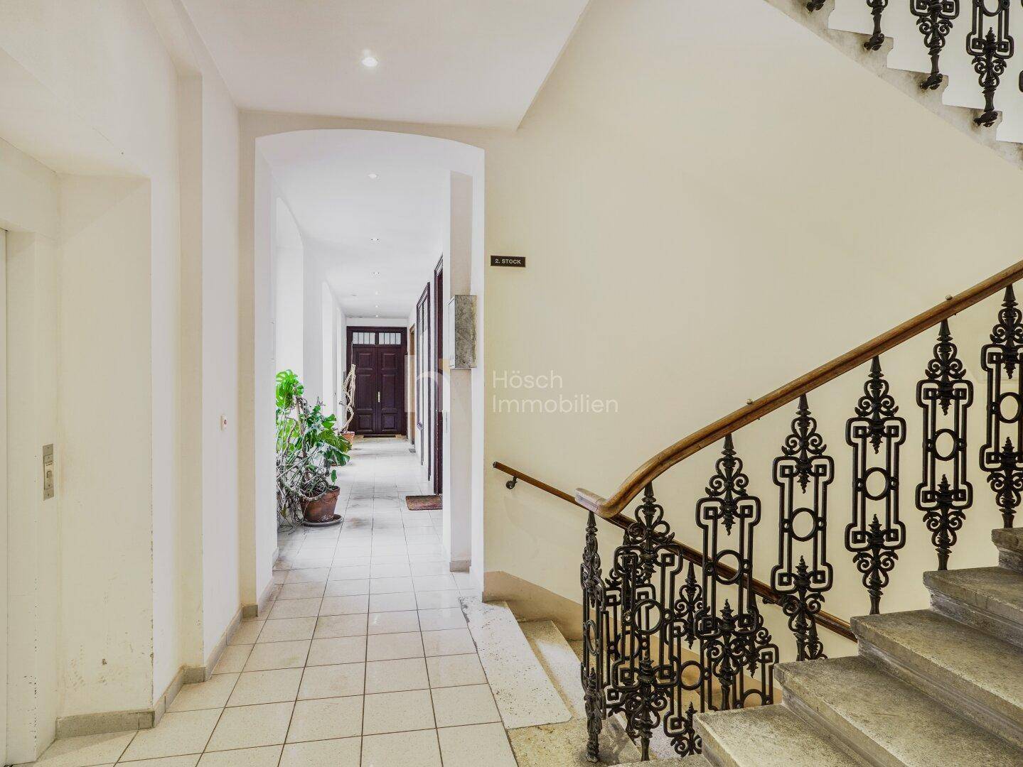 Heller Hausflur mit historischer Treppe, Aufzug und Zugang zu den Wohnungen.
