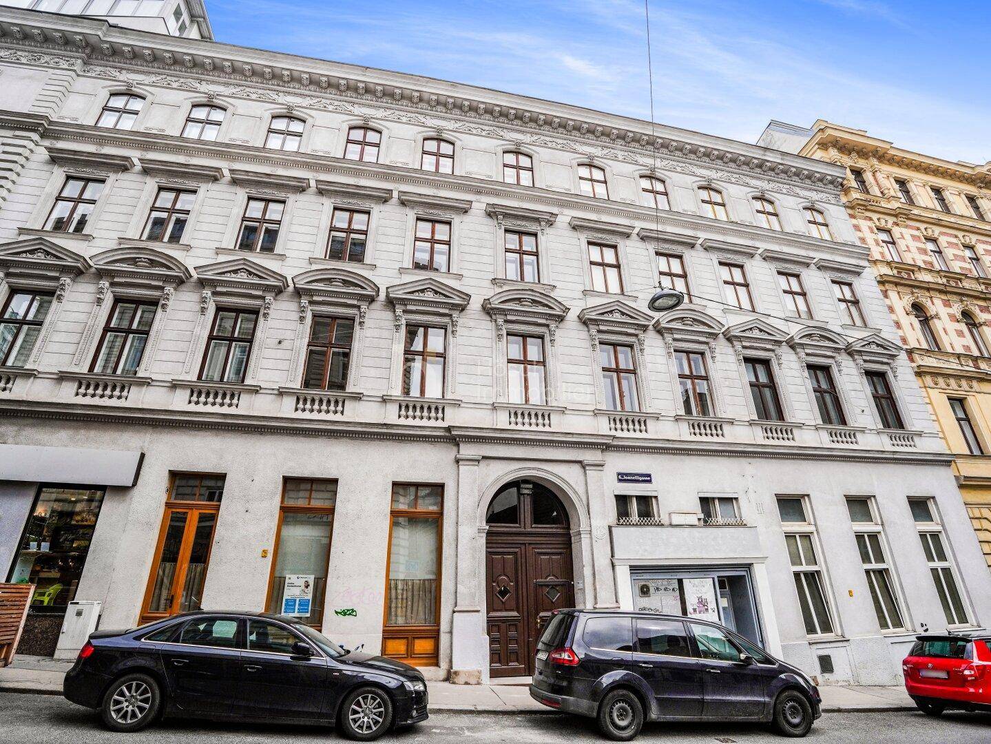 Klassische Fassade eines Wiener Wohnhauses mit vielen Fenstern und parkenden Autos.