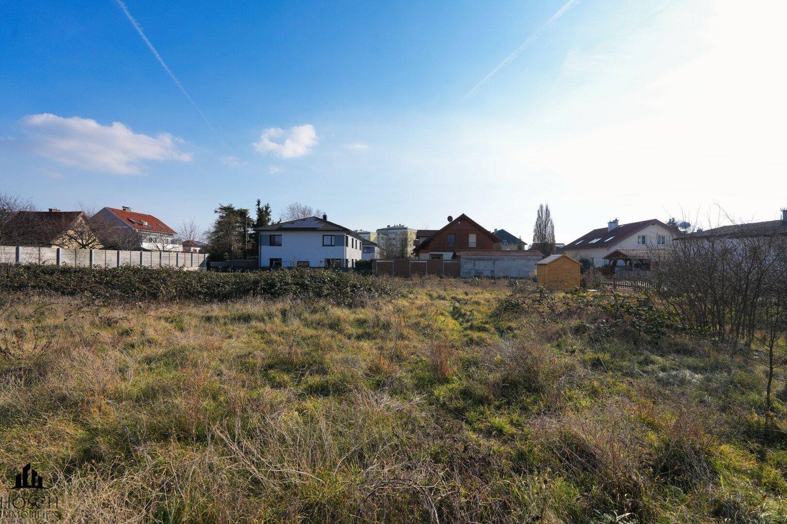 Unbebautes Grundstück mit Blick auf die Nachbarschaft und blauen Himmel.