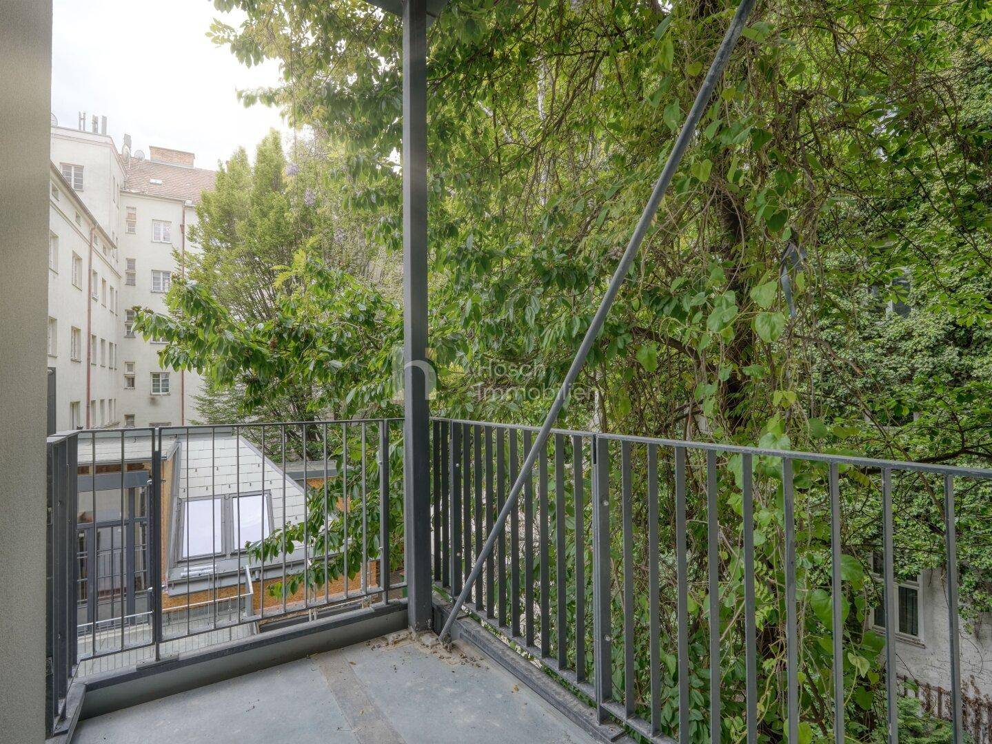 Balkon mit Blick auf einen grünen Innenhof und umliegende Gebäude, bietet eine ruhige Atmosphäre.