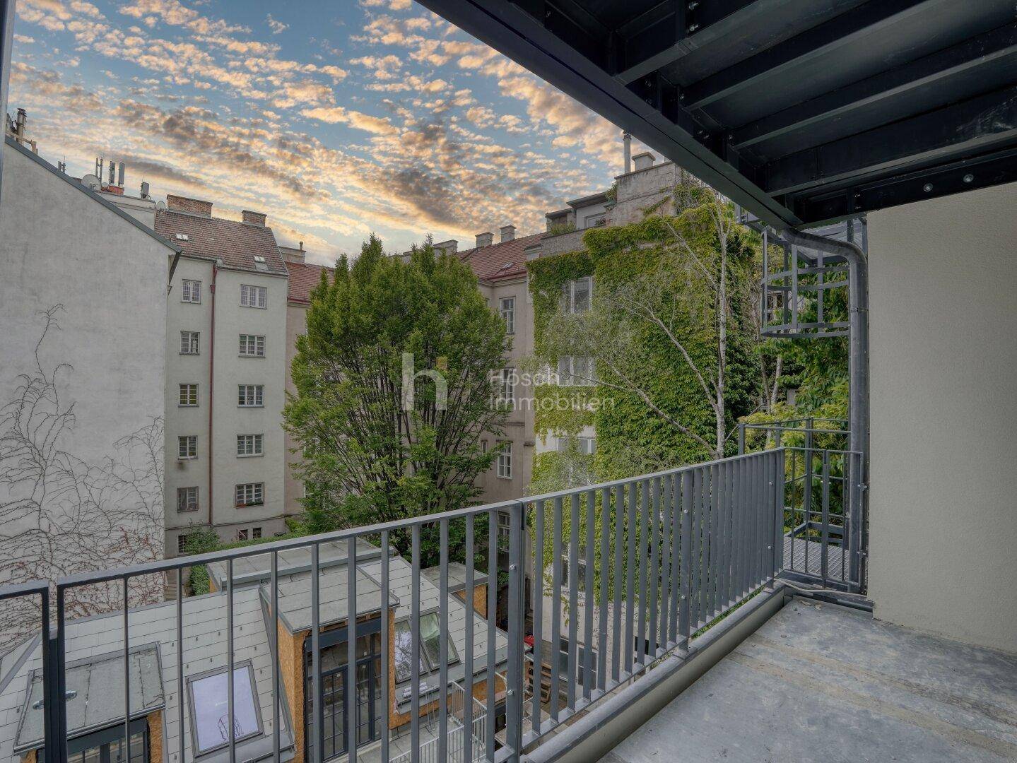 Balkon mit weitem Blick über einen grünen Innenhof und die Stadt, ideal zum Entspannen.