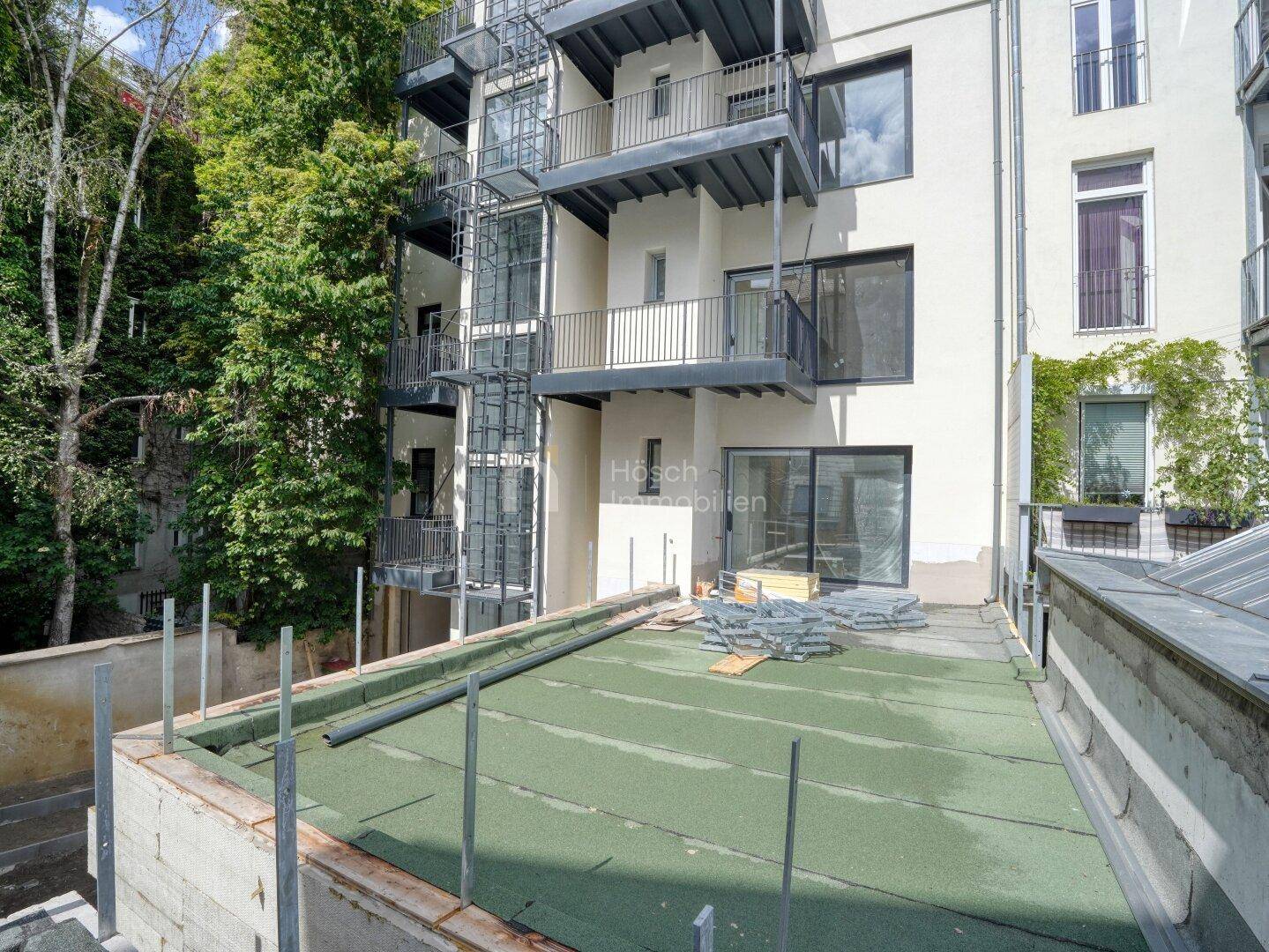 Dachbereich im Bau mit Baumaterialien und Blick auf die Gebäudefassade, zeigt den Fortschritt.