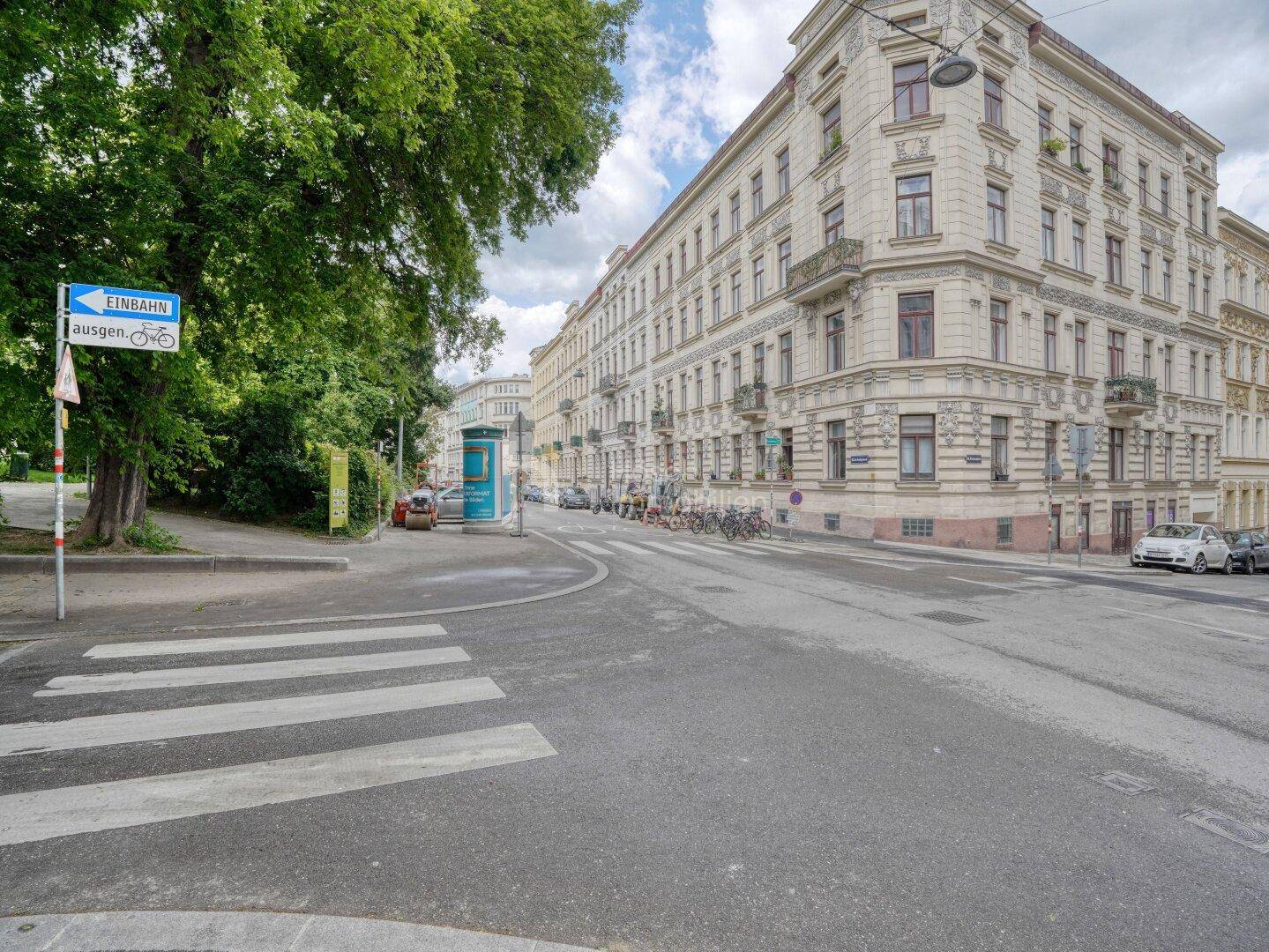 Straßenansicht einer belebten Ecke mit Zebrastreifen und historischen Gebäuden, typisch städtisch.