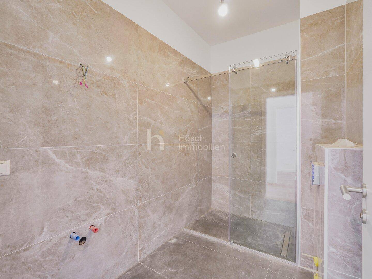 Badezimmer im Bau mit modernen Marmorfliesen und einer Duschkabine, hochwertig ausgestattet.