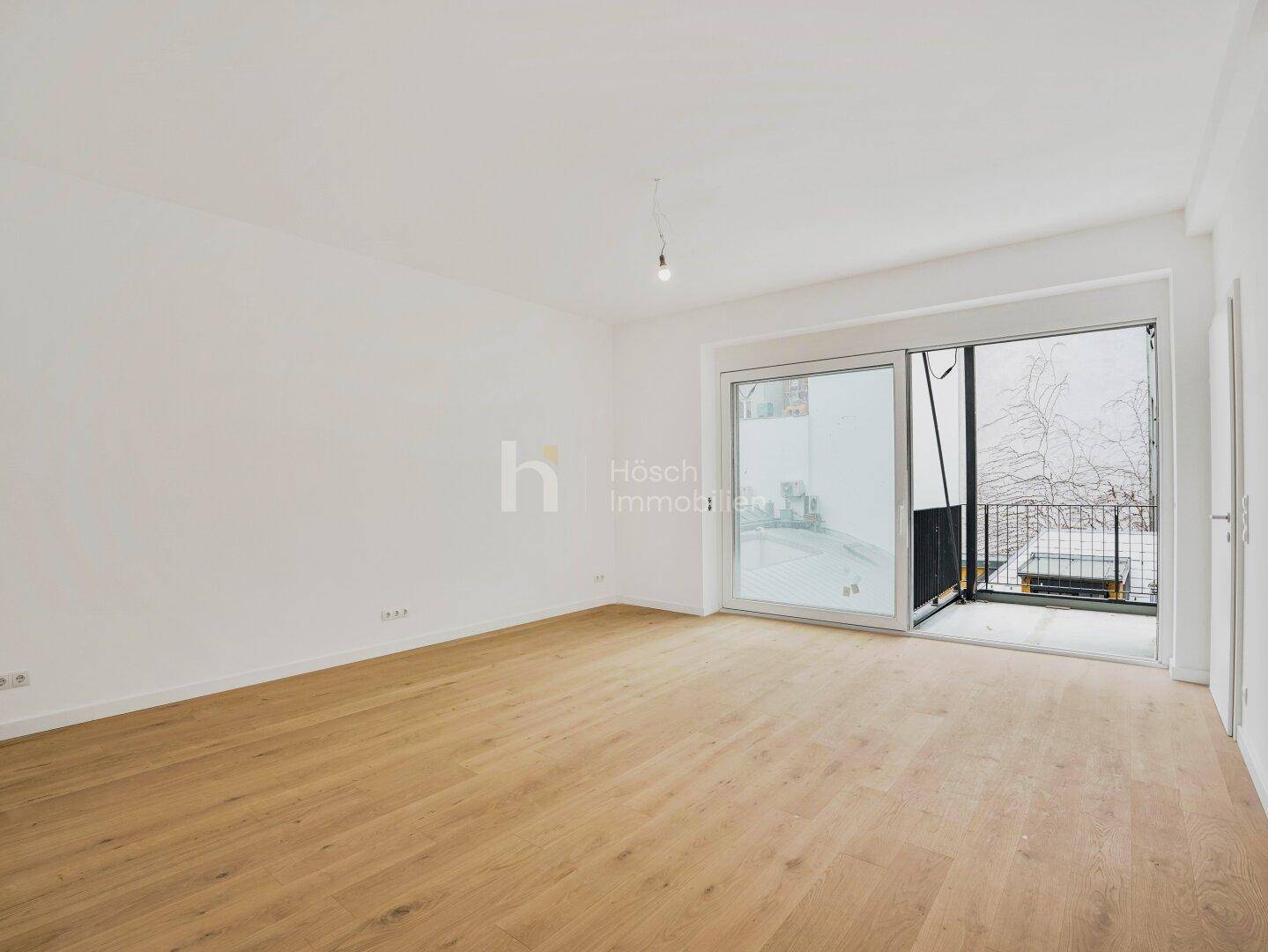 Leeres Wohnzimmer mit Holzboden und großen Schiebetüren zum Balkon, hell und geräumig.