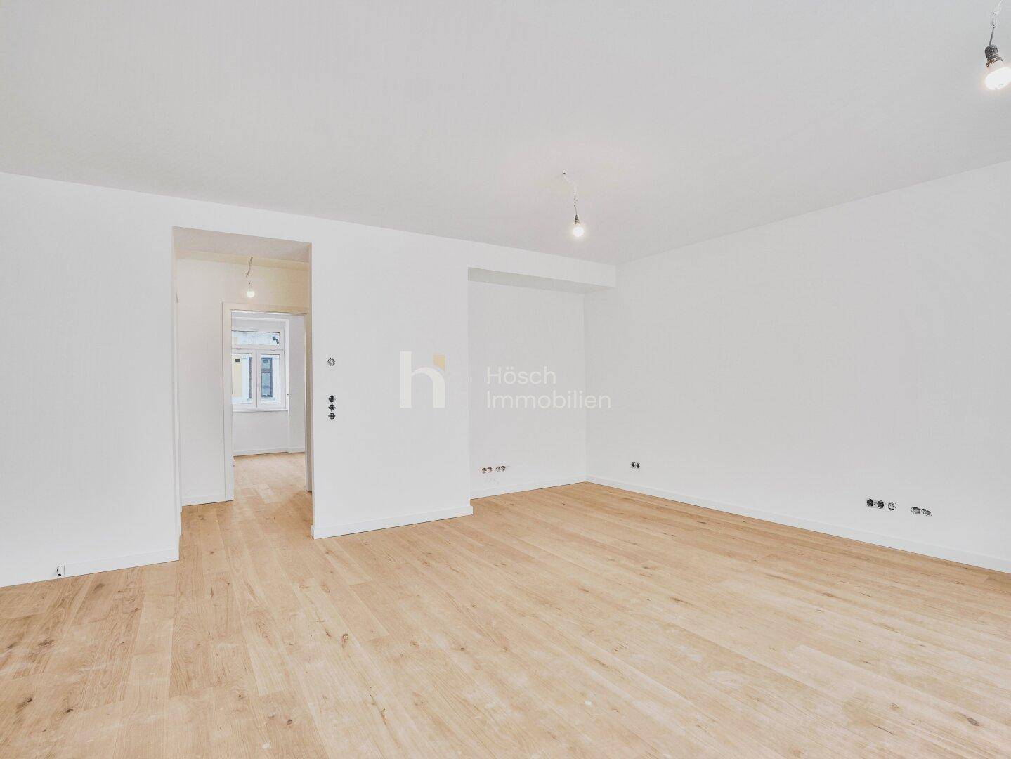 Geräumiger, heller Raum mit Holzboden und offenem Übergang zu weiteren Bereichen der Wohnung.