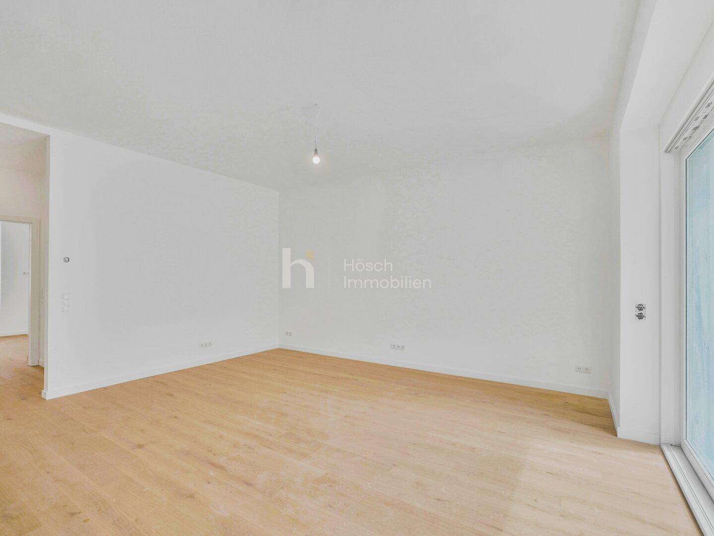Helles Zimmer mit Holzboden und großer Schiebetür, die Zugang zu einem Außenbereich ermöglicht.