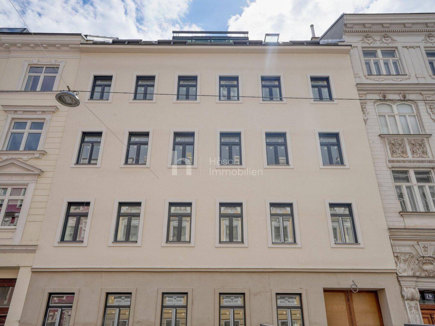 Die moderne Fassade des Mehrfamilienhauses mit zahlreichen Fenstern und einem Dachaufbau.