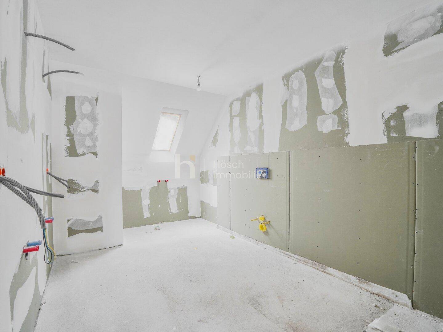 Unfertiges Badezimmer mit vorbereiteten Installationen, Dachfenster und Rohbauwänden.