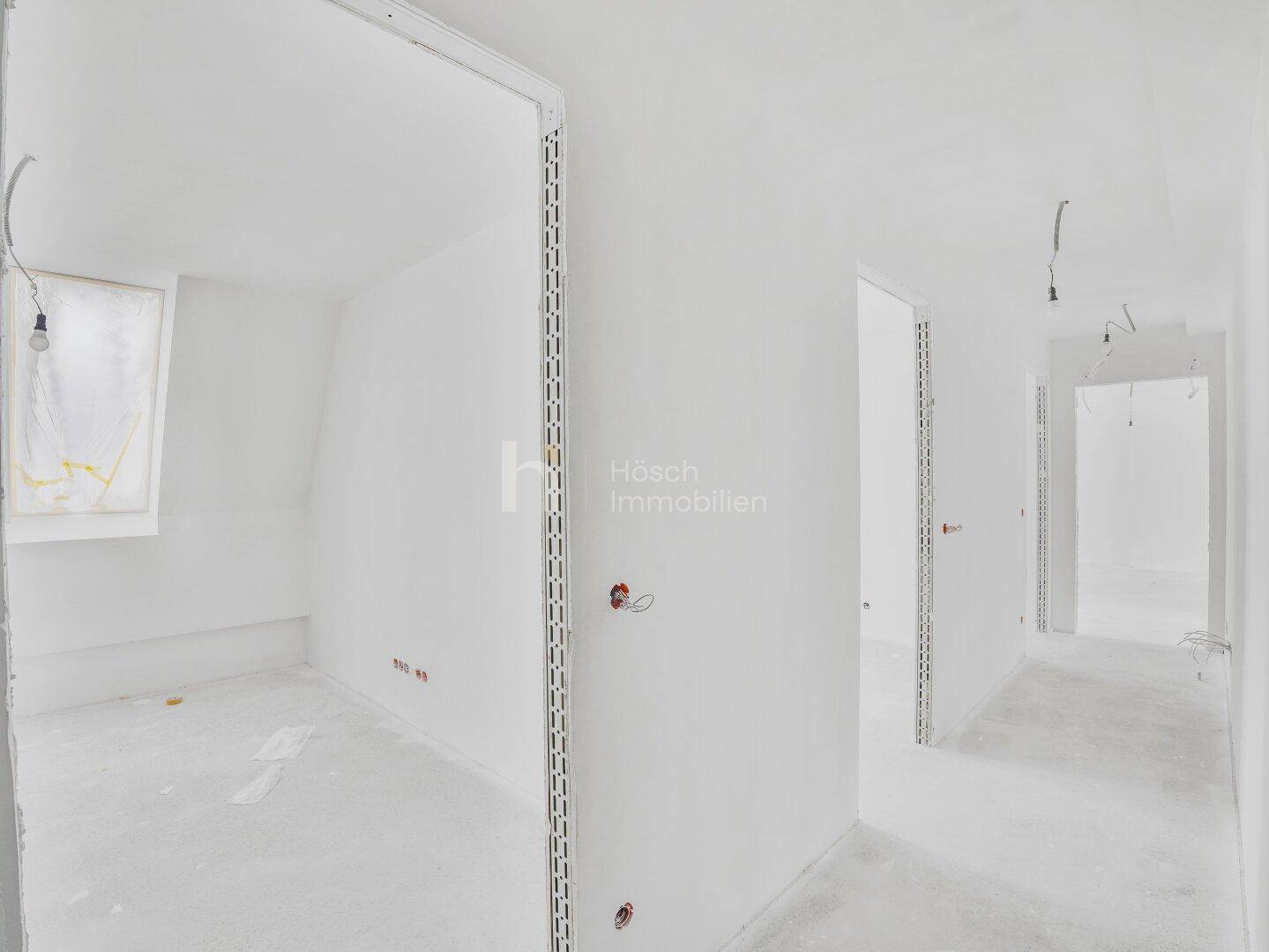 Heller Flur im Rohbauzustand mit mehreren Türöffnungen und einem Fenster.
