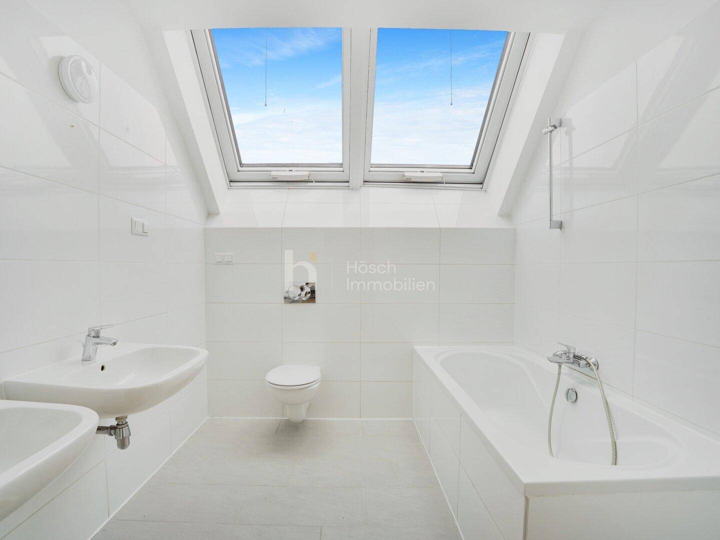 Helles Badezimmer mit Badewanne, Waschbecken, Toilette und zwei Dachfenstern für viel Tageslicht.