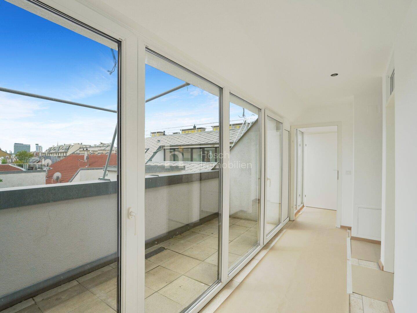 Heller Innenraum mit großen Fensterfronten und Blick auf die Stadt, der zu einer Terrasse führt.