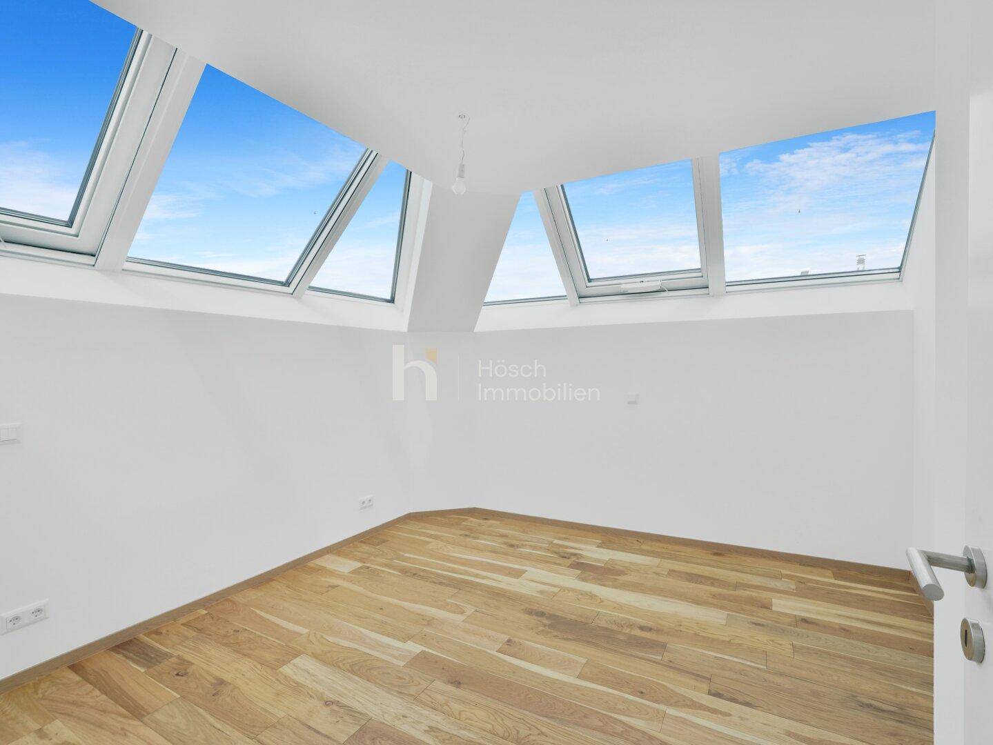 Lichtdurchfluteter Dachgeschossraum mit mehreren Dachfenstern und Holzboden.