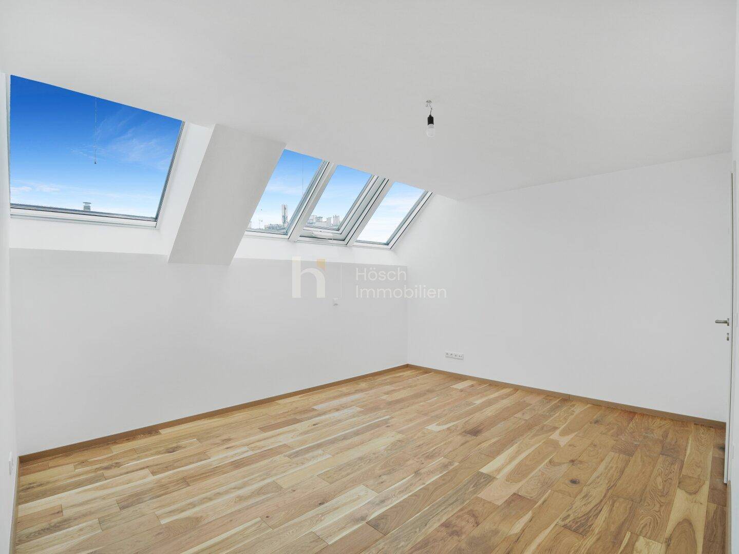 Unmöblierter Raum im Dachgeschoss mit Holzboden und mehreren großen Dachfenstern.