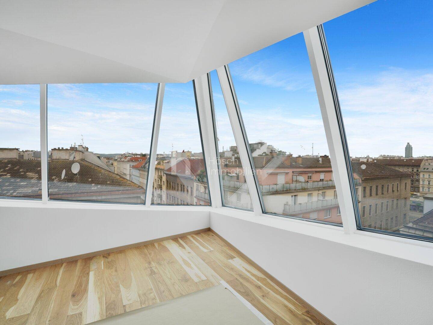 Heller Raum im Dachgeschoss mit schrägen Fenstern und weitem Blick über die Stadt.