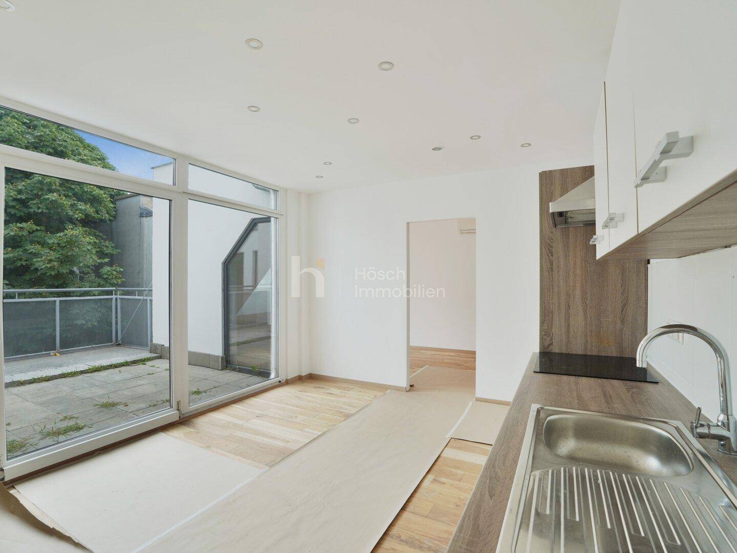 Moderne Küche mit Spüle, Holz-Arbeitsplatte und Zugang zu einem Balkon mit Blick ins Grüne.