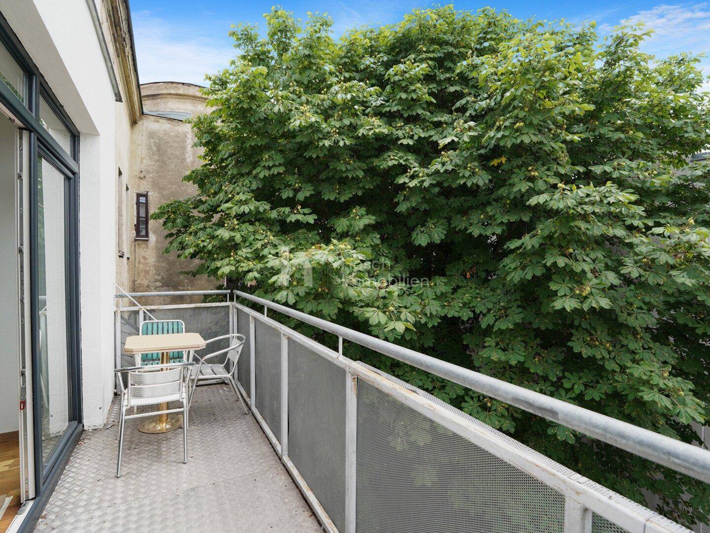 Gemütlicher Balkon mit kleinem Tisch und Stühlen, umgeben von viel Grün.