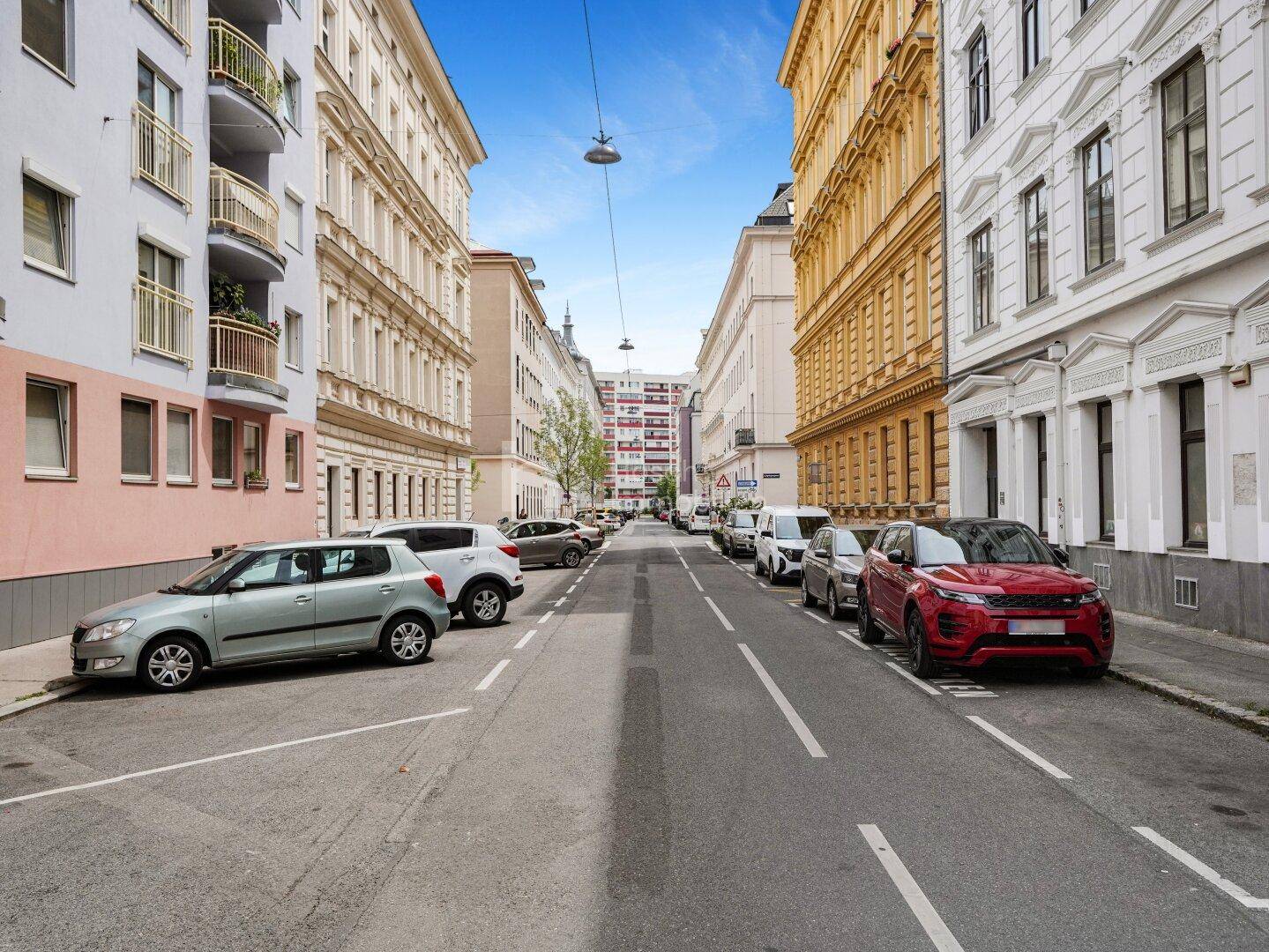 Eine belebte Straße in einem Stadtviertel mit geparkten Autos und historischen Gebäuden.