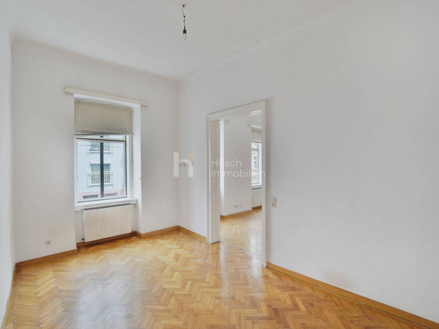 Helles Zimmer mit klassischem Fischgrätparkett und einem Fenster, das den Raum gut belichtet.