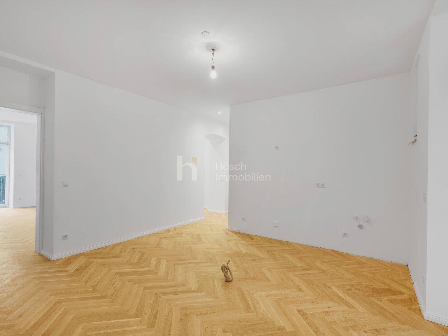Heller Wohnbereich mit Fischgrätparkett und weißen Wänden, bereit für individuelle Gestaltung.
