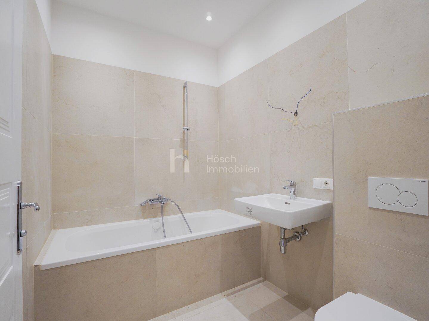 Modernes Badezimmer mit Badewanne, Wand-WC und beigefarbenen Fliesen an Wänden und Boden.