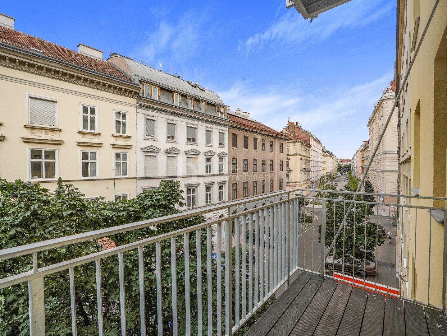 Balkon mit Holzboden und Blick auf die belebte Stadtstraße mit Bäumen und Gebäuden.