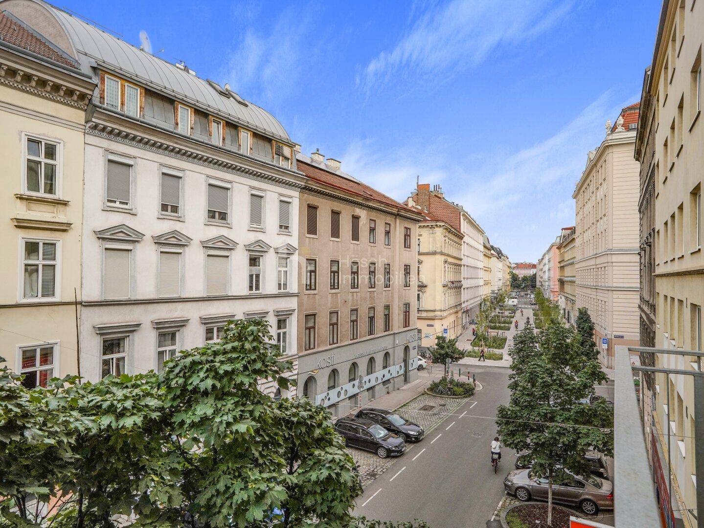 Weitblick von einem Balkon auf eine belebte Stadtstraße mit Bäumen und historischen Gebäuden.