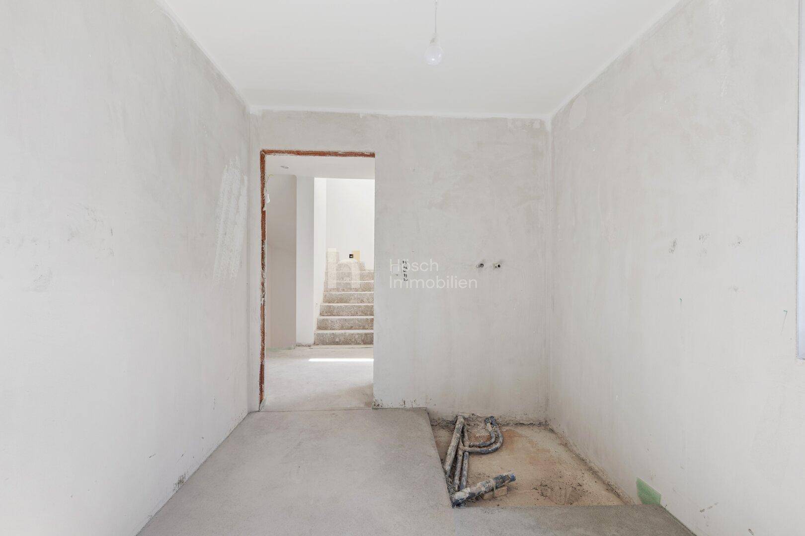 Unfertiger Raum mit Türöffnung zum Treppenhaus und Rohbau-Boden in einem Neubau.