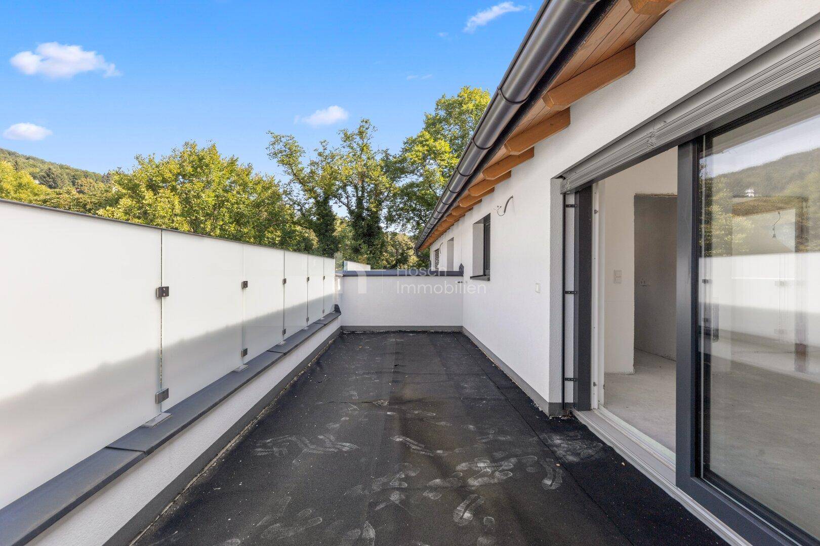 Unfertiger Balkon mit Glasbrüstung und Blick auf die grüne Umgebung.