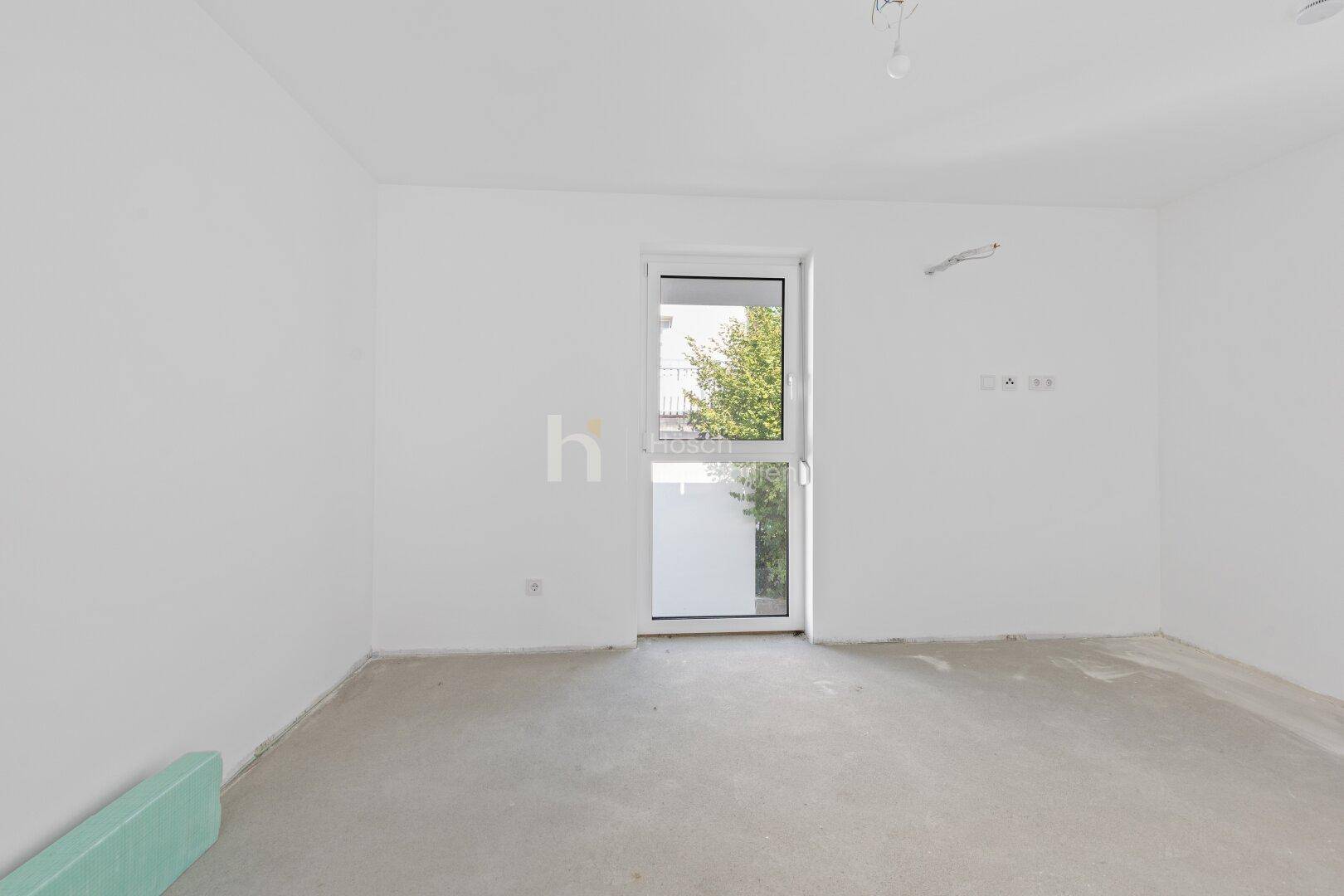 Unfertiges Schlafzimmer mit Zugang zum Außenbereich und Rohbau-Boden in einem Neubau.