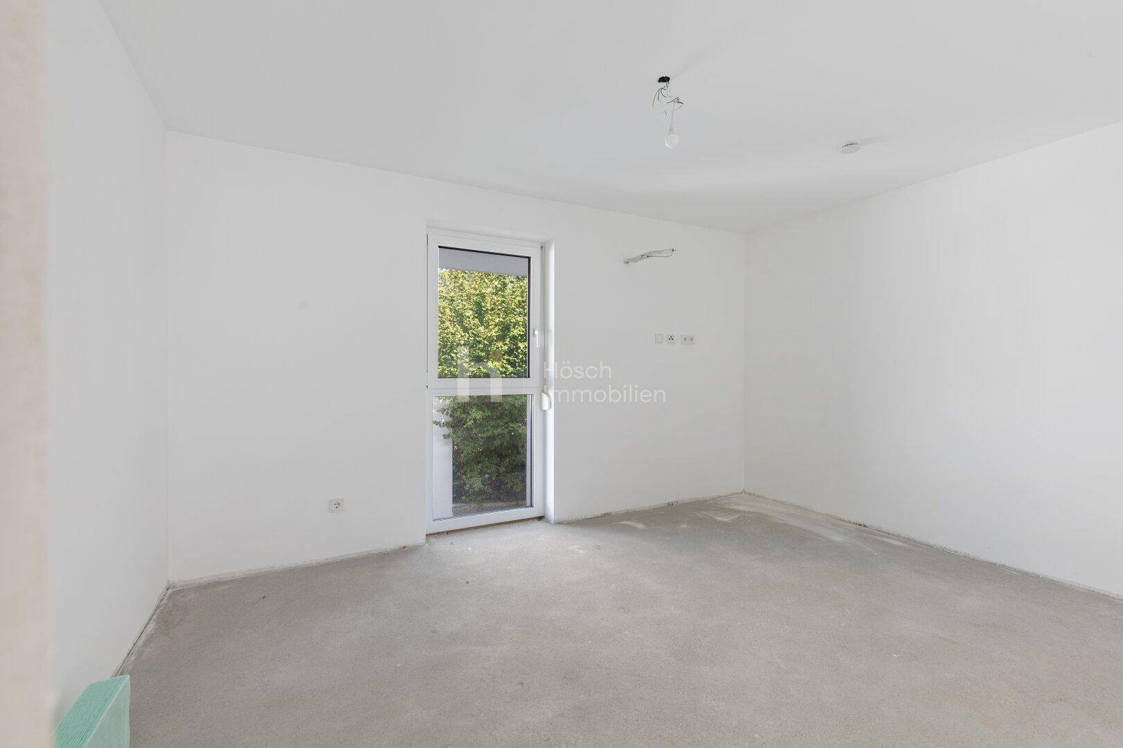 Helles, unfertiges Schlafzimmer mit Fenster und Rohbau-Boden in einem Neubau.