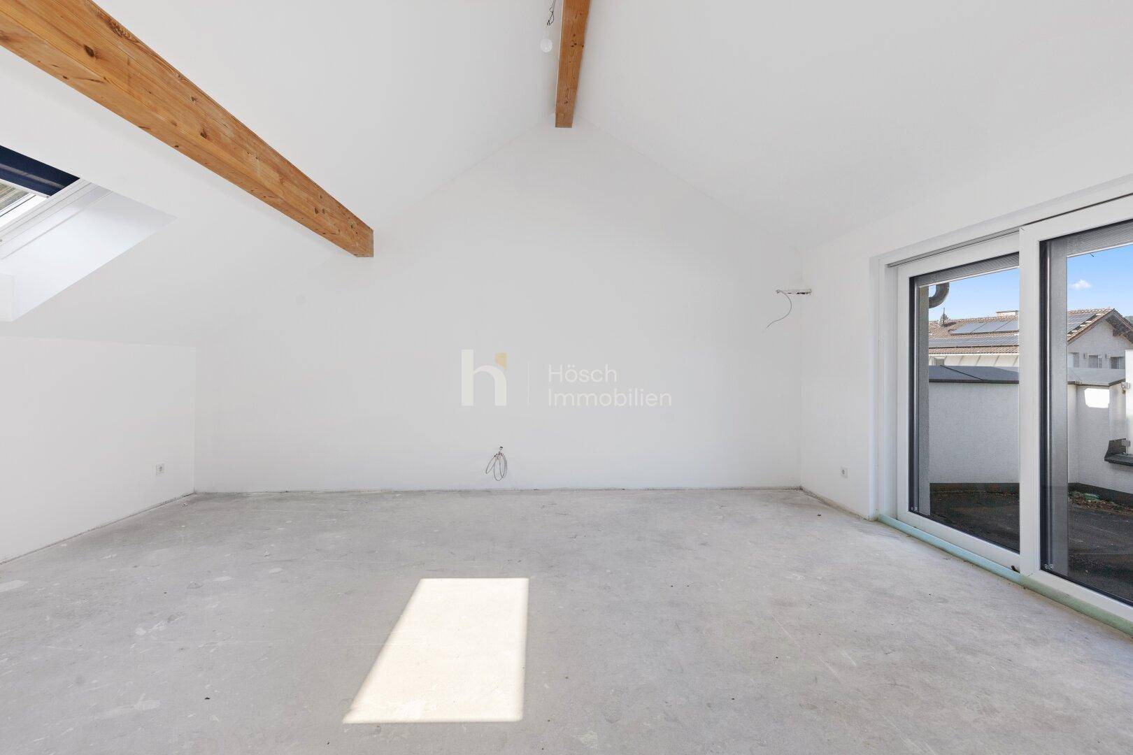 Geräumiger, unfertiger Dachbodenraum mit Schiebetür und Rohbau-Boden in einem Neubau.