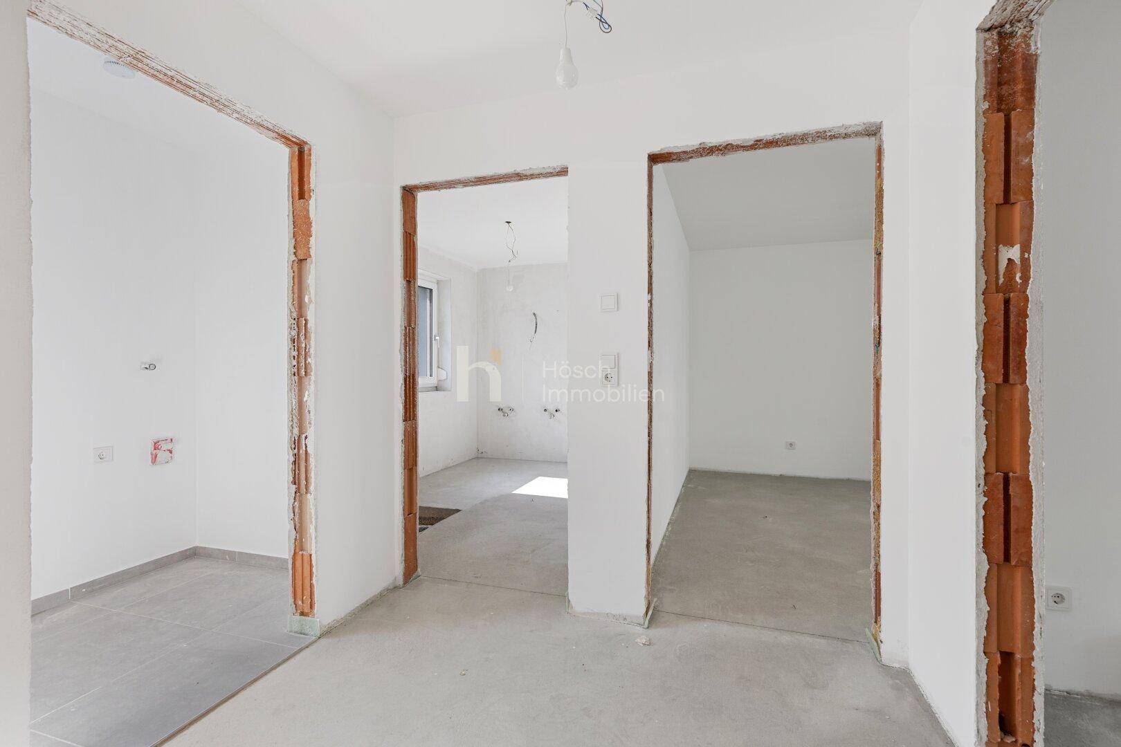 Unfertiger Flur mit mehreren Türöffnungen und Rohbau-Boden in einem Neubau.