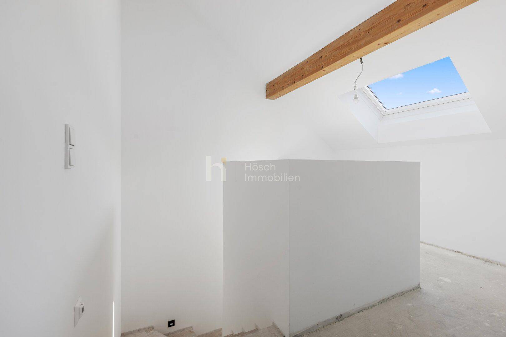 Unfertiger Dachbodenraum mit sichtbaren Holzbalken und einem Dachfenster für natürliches Licht.