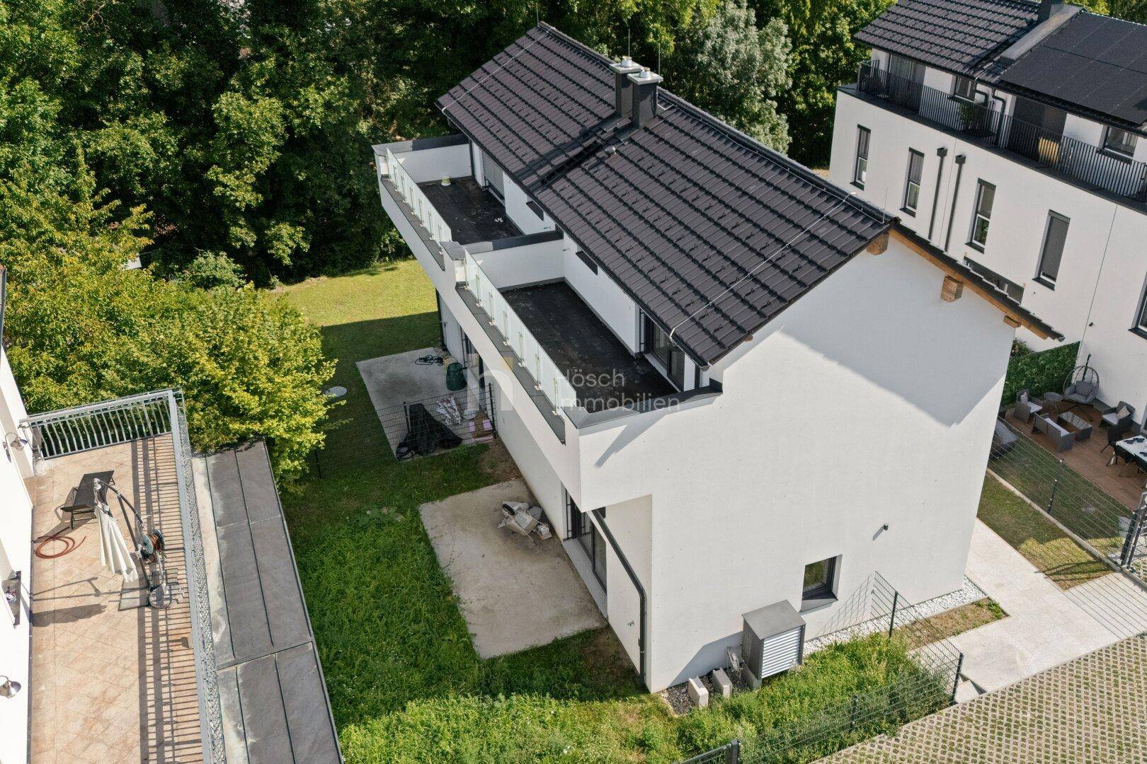 Luftaufnahme eines modernen Einfamilienhauses mit dunklem Dach und Gartenbereich.