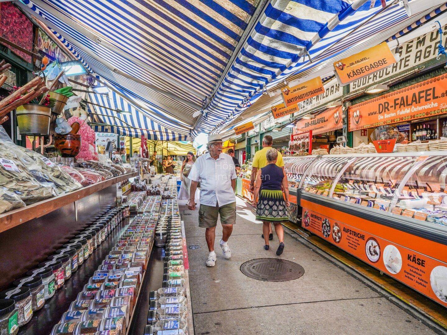 Buntes Markttreiben mit verschiedenen Ständen, Produkten und vielen Besuchern unter gestreiften Markisen.