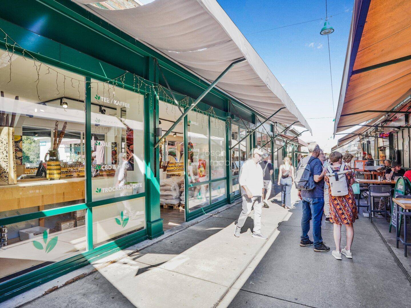 Belebtes Marktgeschehen vor der grünen Ladenfassade mit Passanten und weiteren Marktständen.