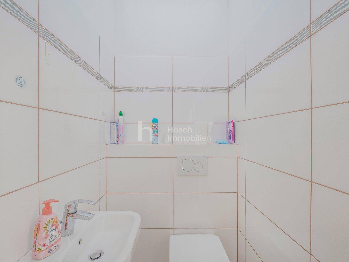 Kleines, hell gefliestes Gäste-WC mit wandhängender Toilette und einem kleinen Waschbecken.