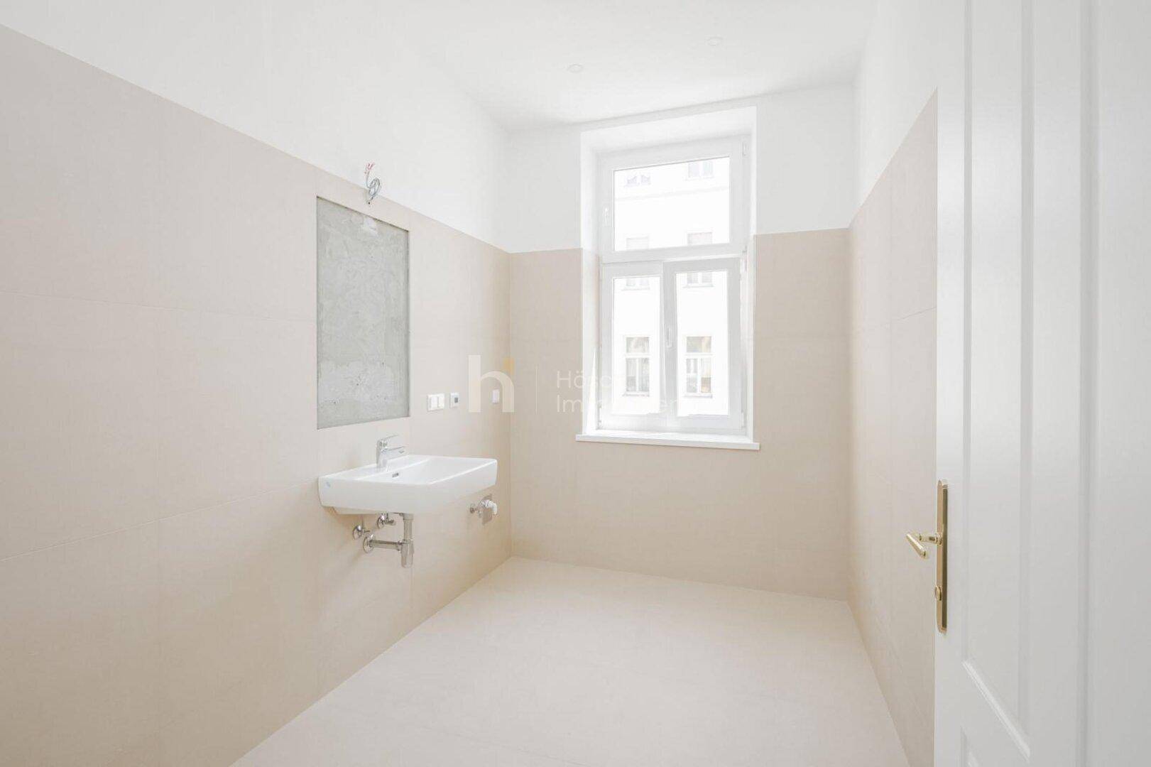 Modernes Badezimmer mit beigefarbenen Fliesen, einem Waschbecken und einem Fenster.
