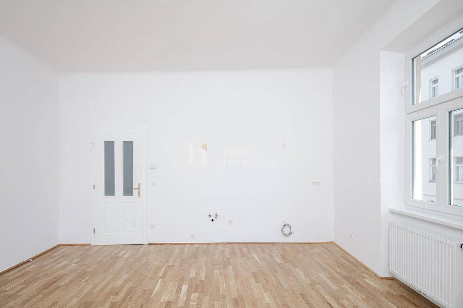 Leerer Raum, vorbereitet für eine Küche, mit Parkettboden und einem Fenster.