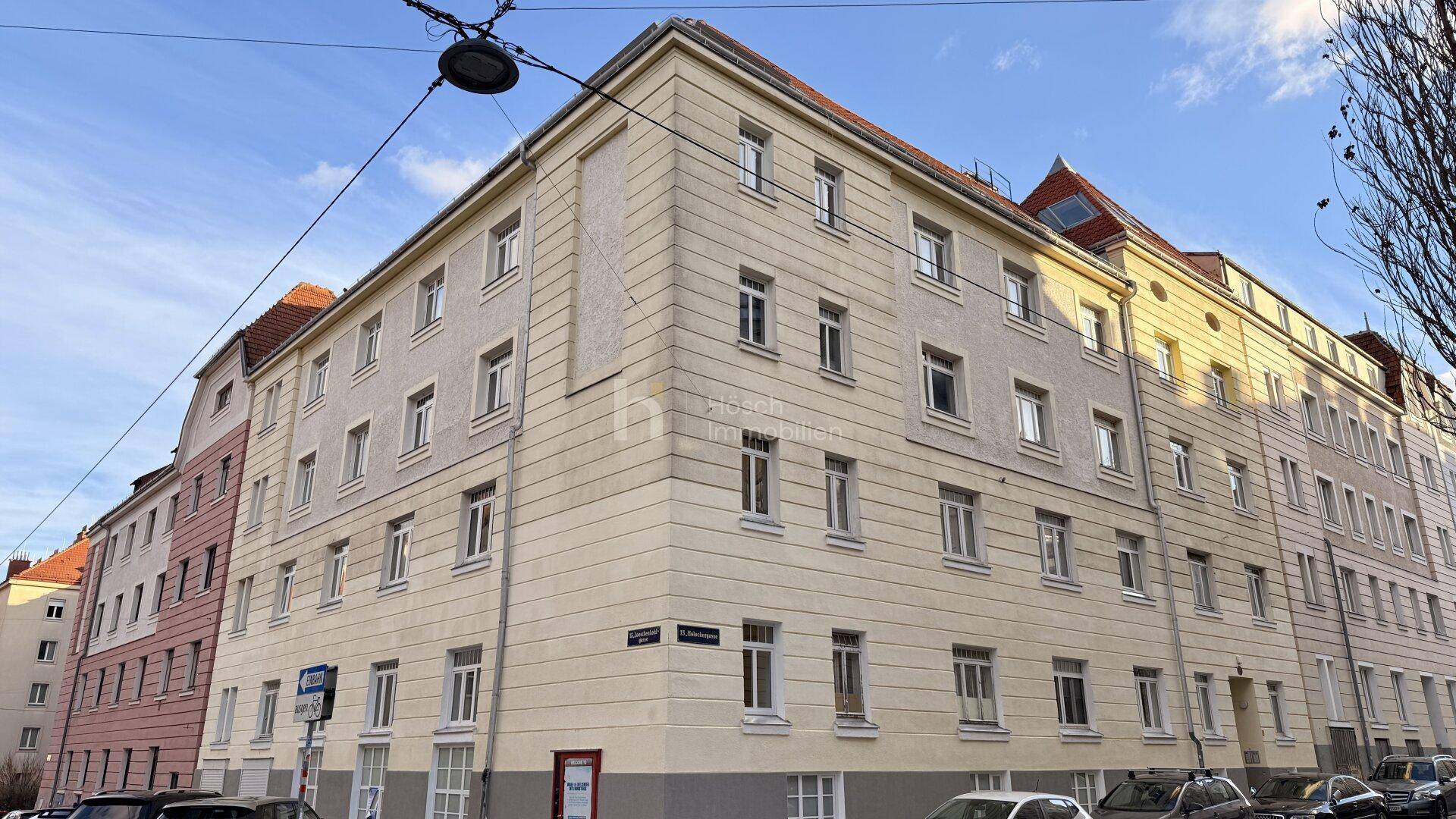 Historisches Eckgebäude mit klassischer Fassade und vielen Fenstern unter blauem Himmel.