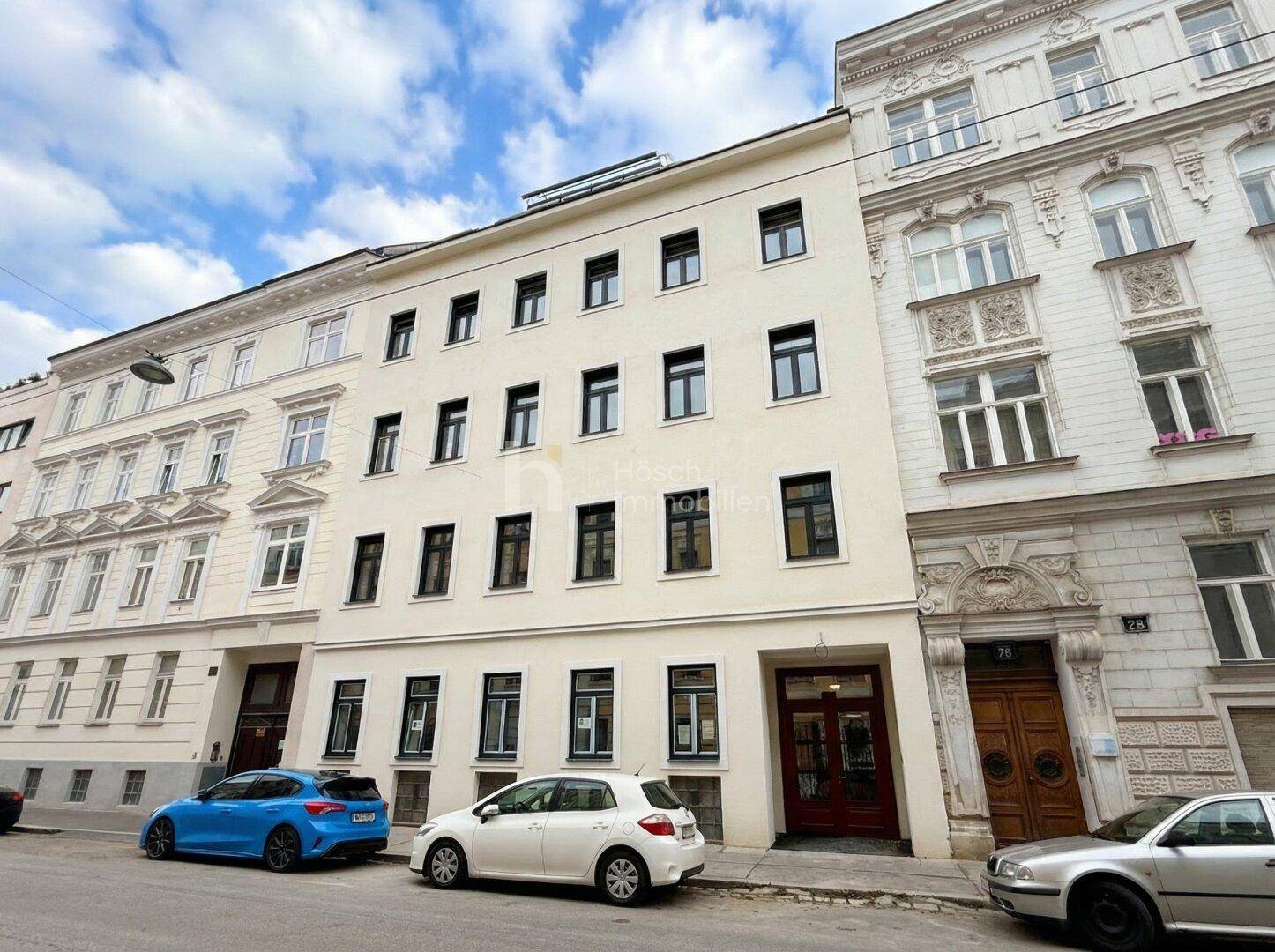 Straßenansicht eines Mehrfamilienhauses mit klassischer Fassade und parkenden Autos davor.