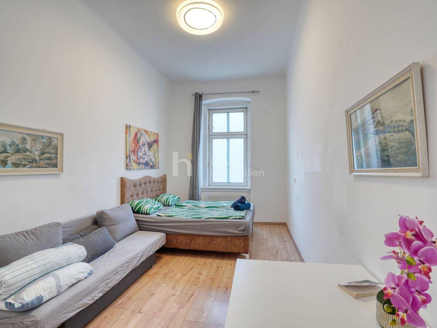 Gemütliches Schlafzimmer mit Holzboden, Bett und Sofa, dekoriert mit Kunstwerken.