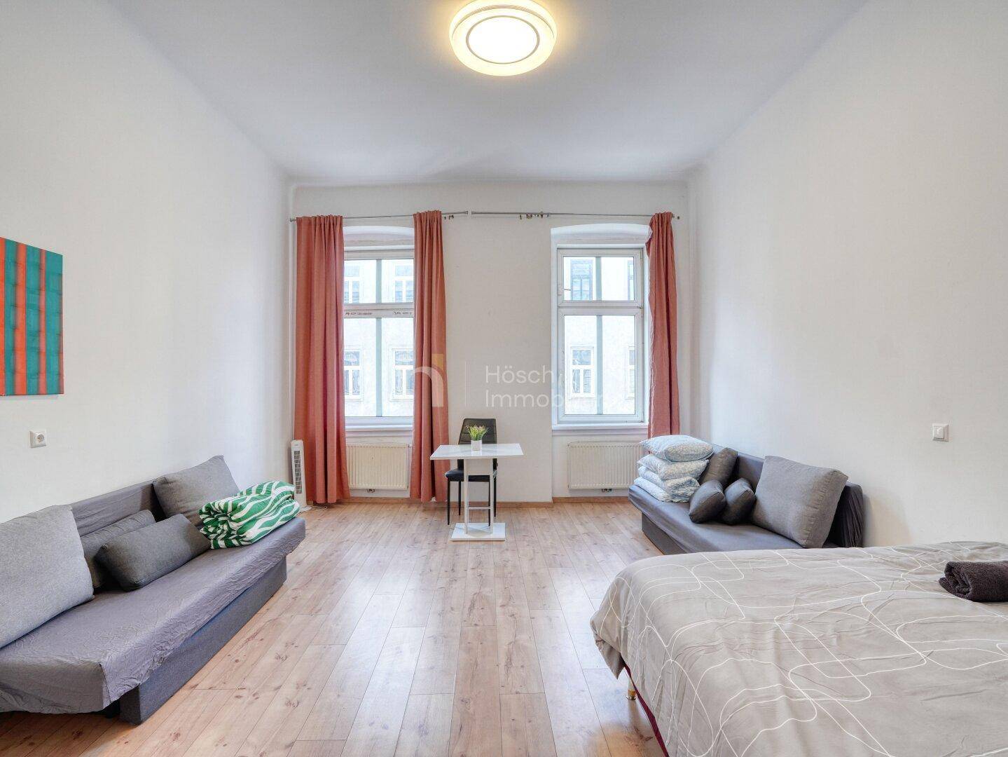 Lichtdurchflutetes Schlafzimmer mit Holzboden, bequemen Sofas und einem kleinen Esstisch.