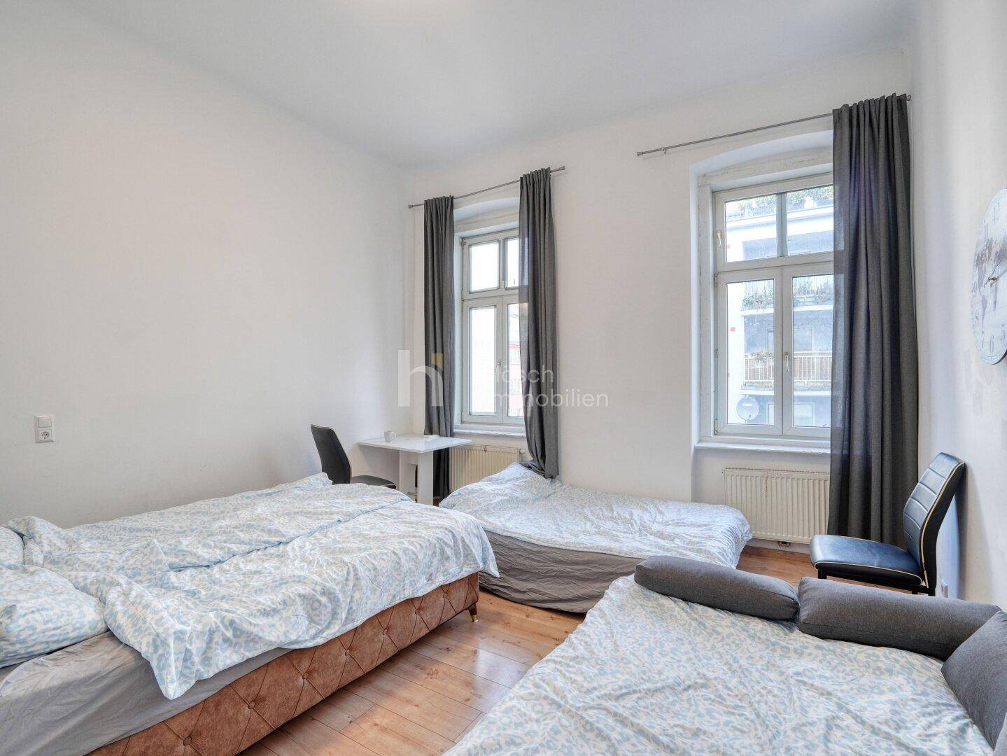 Geräumiges Schlafzimmer mit drei Betten, Holzboden und großen Fenstern.