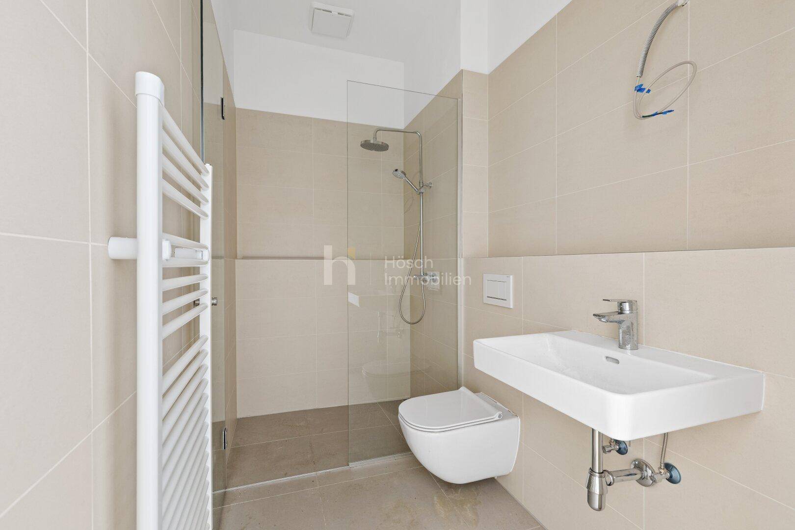 Modernes Badezimmer mit beigefarbenen Fliesen, bodengleicher Dusche und wandhängendem WC.