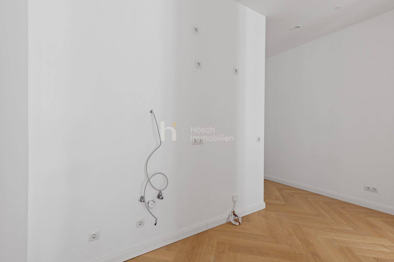 Heller Flurbereich mit Fischgrätparkett und vorbereiteten Anschlüssen für Wandinstallationen.