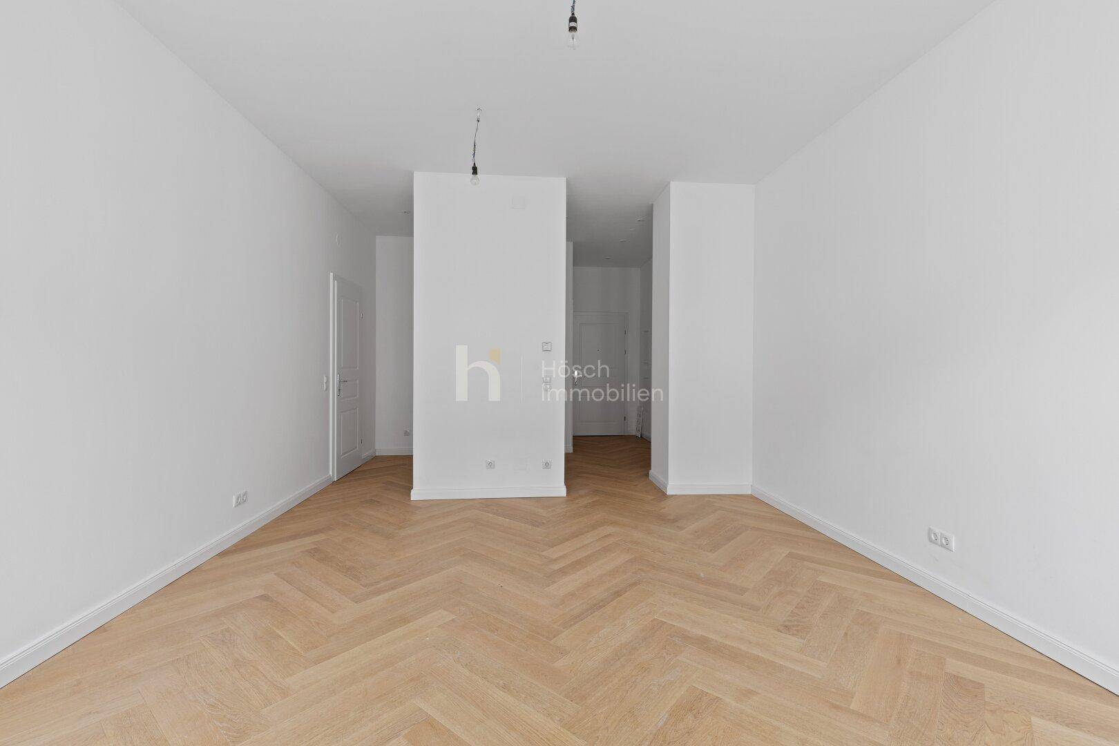 Geräumiges, leeres Zimmer mit Fischgrätparkett und zwei tragenden Säulen, bereit zur Einrichtung.